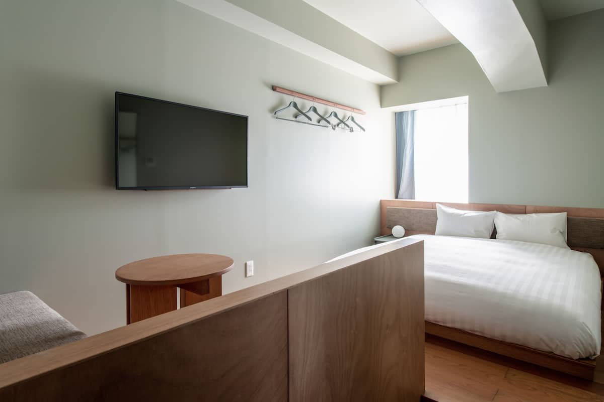 A modern hotel room with a large bed, a flat-screen TV mounted on the wall, a small wooden table, and a seating area with a cushioned bench.
