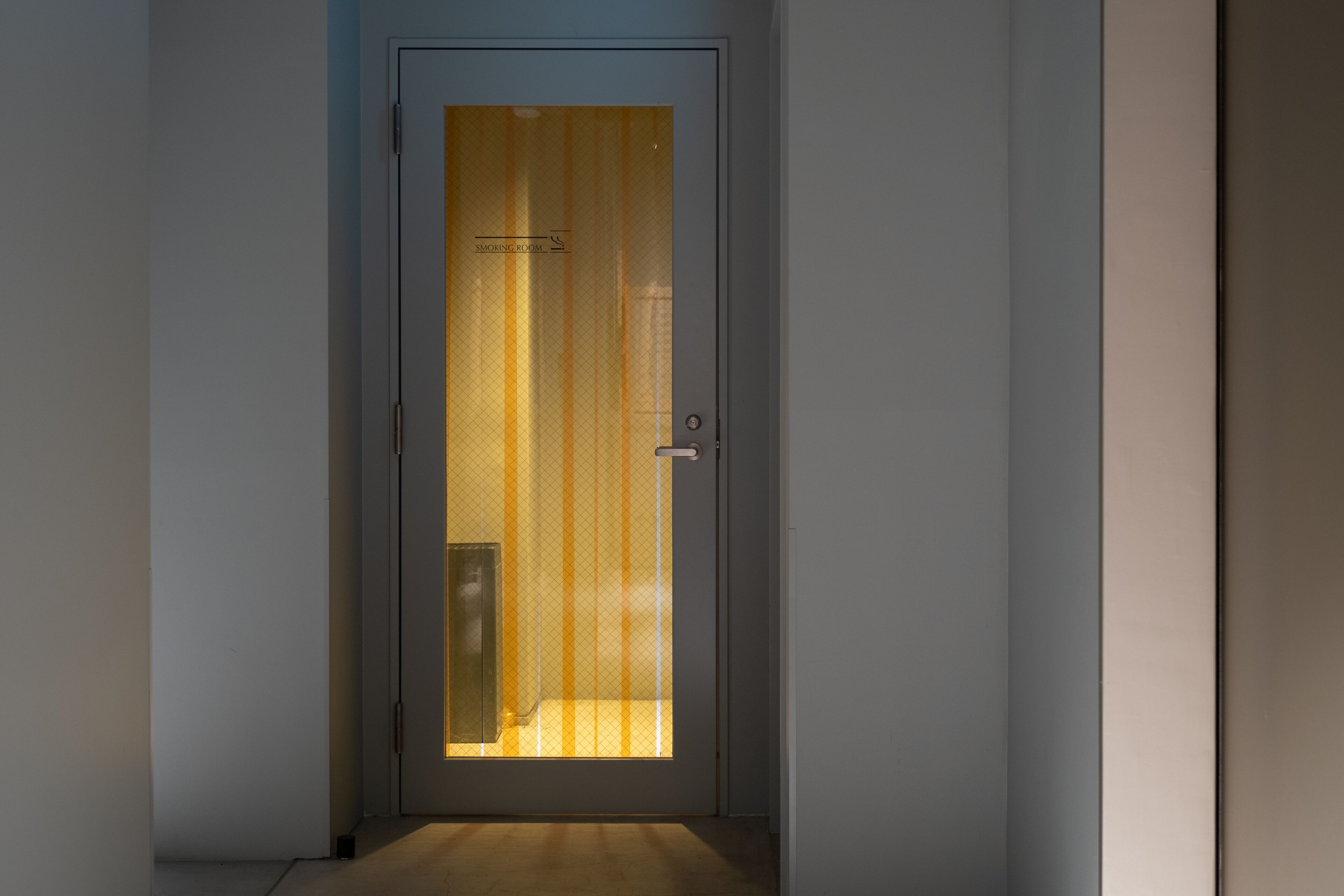 A narrow hallway leading to a door with a frosted glass panel and a sign indicating a smoking room.
