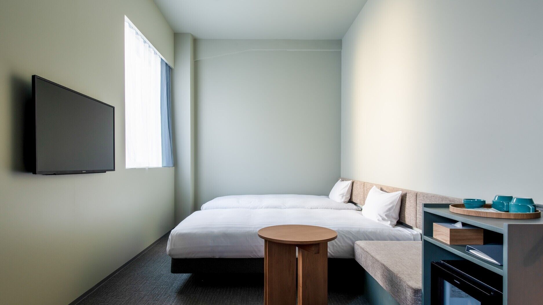 Een hotelkamer met een bed, een televisie, een klein rond tafeltje en een kitchenette.