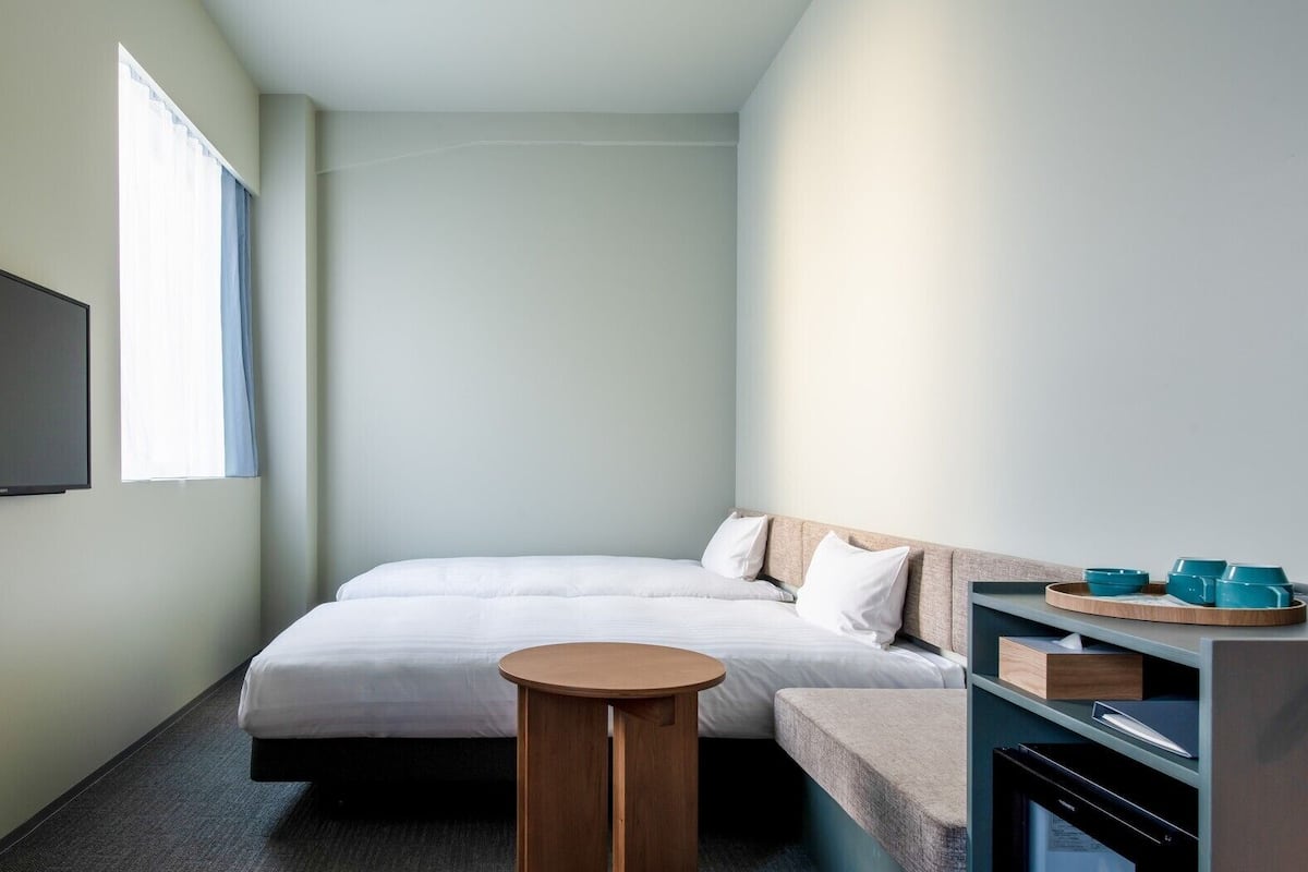 A hotel room with a bed, a TV, a small round table, and a kitchenette area.