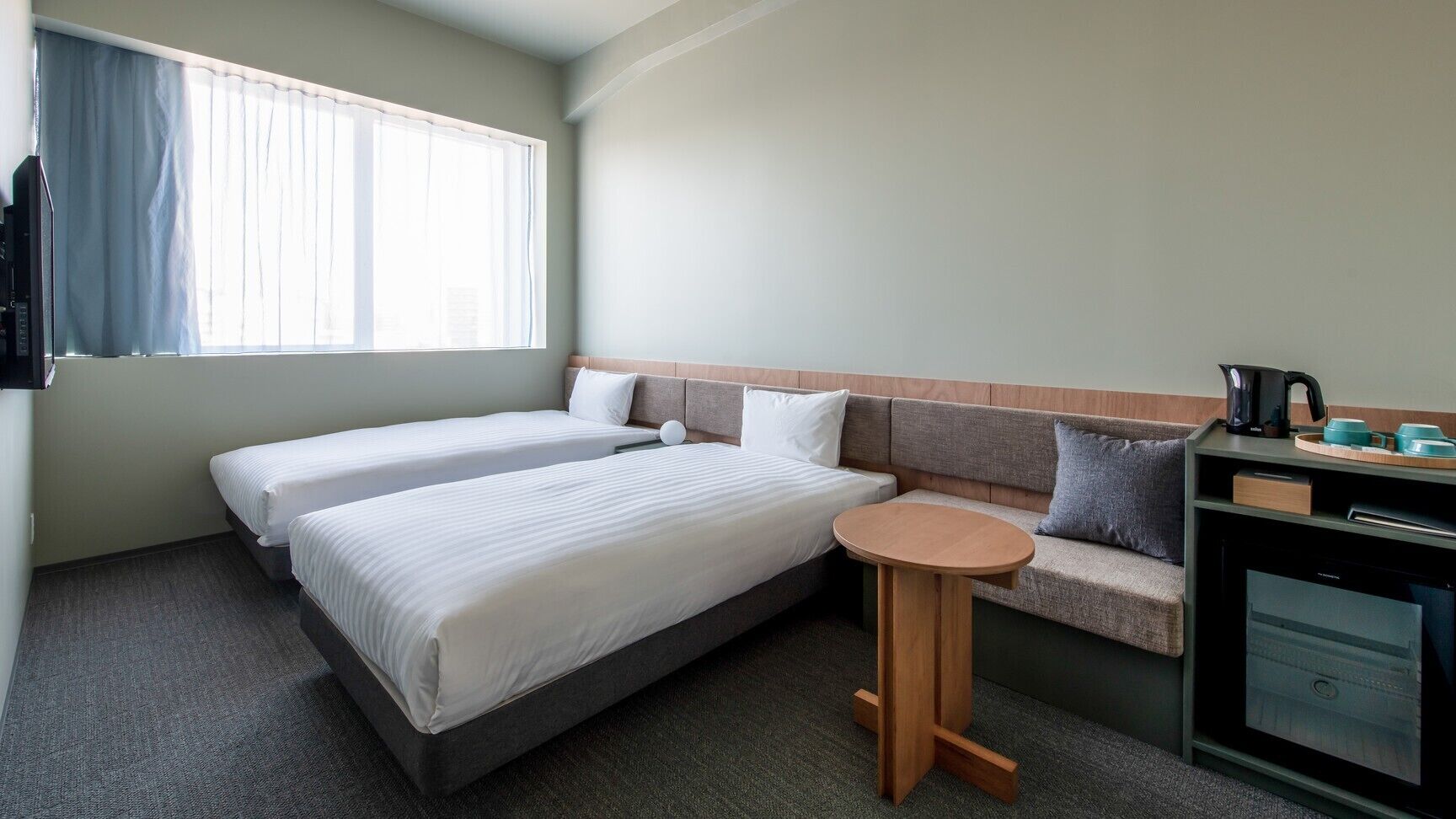 Hotelkamer met twee bedden, een klein rond tafeltje, een bank, een bureau met waterkoker en een koffiezetapparaat.