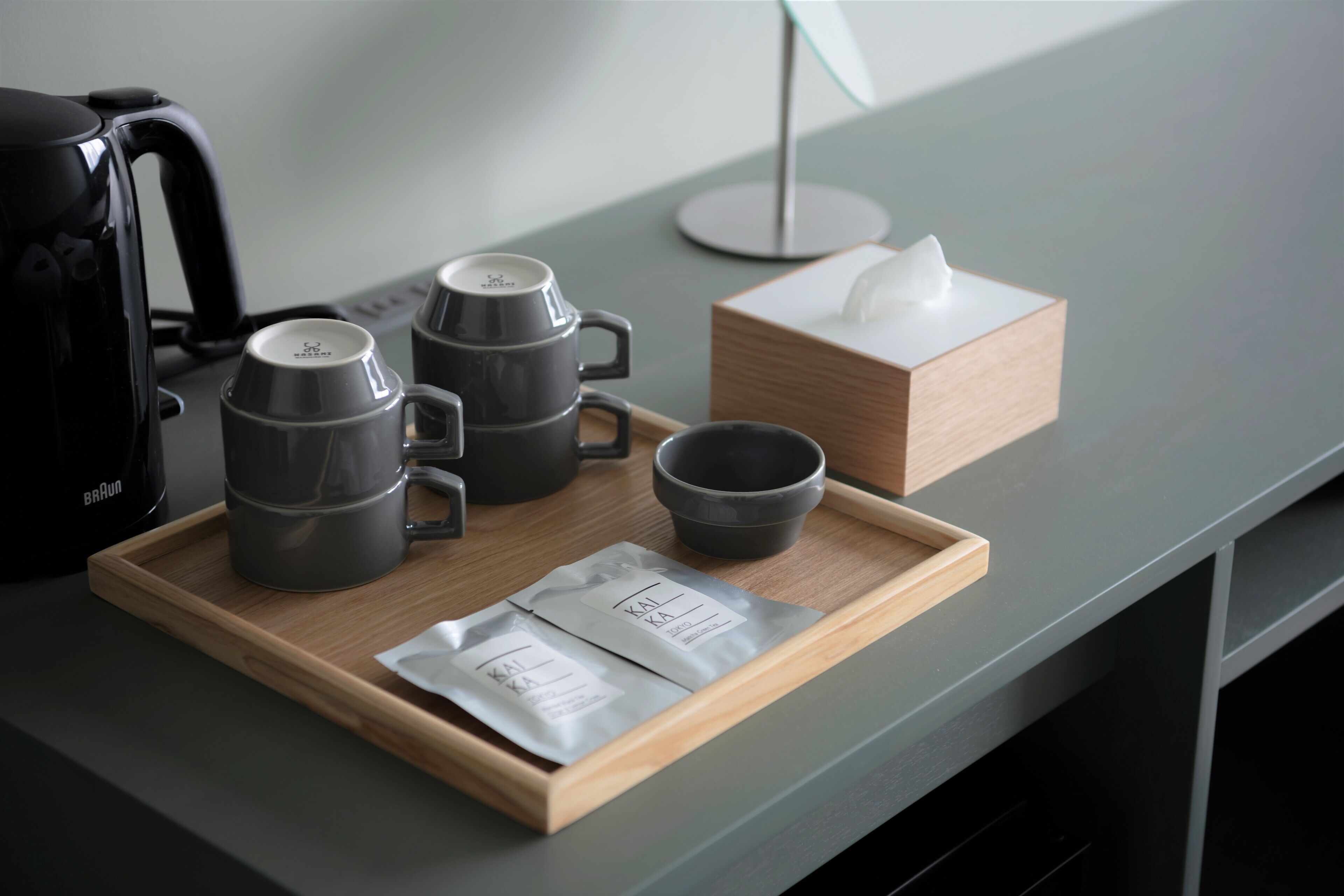 A tray with three grey mugs, a black coffee pot, and a tissue box on a grey countertop.