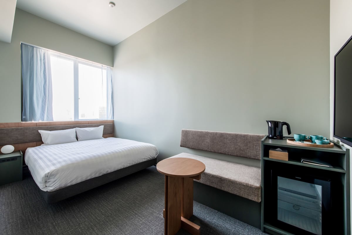 A hotel room with a bed, a small wooden stool, a sofa, a TV, and a coffee maker.