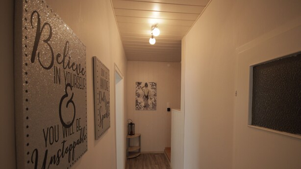 A hallway with a wooden floor, a light fixture, and various wall decorations including motivational quotes and a black and white artwork. - Apartment Come-Home (Hohnstedt)