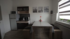 A compact kitchen with a refrigerator, microwave, and coffee maker. There are three framed pictures on the wall and a window with blinds. - Apartment Come-Home (Hohnstedt)