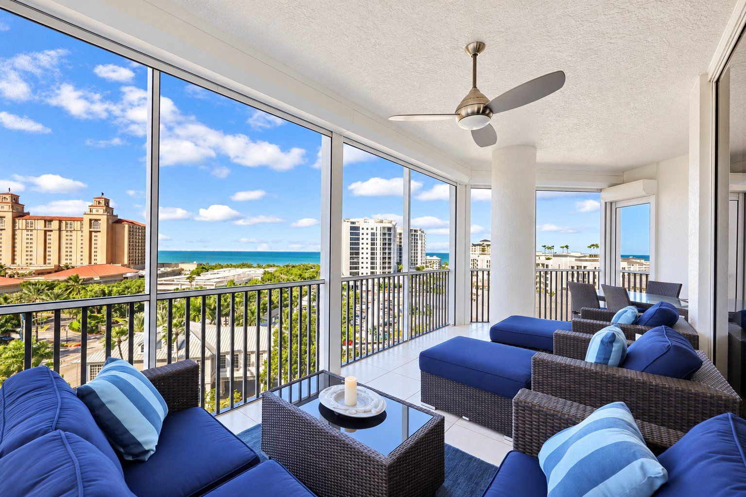 A balcony with wicker furniture and a view of the ocean and buildings.