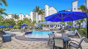 A pool area with lounge chairs, umbrellas, and a stone-tiled patio. - Regatta - Breathtaking Gulf and Bay Views! (Naples)