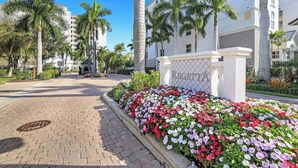 A gated entrance with a sign reading 'KEGATTA,' palm trees, and a paved walkway leading to a building. - Regatta - Breathtaking Gulf and Bay Views! (Naples)
