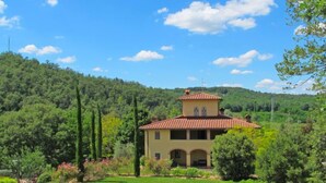 Una villa con techo de tejas rojas, rodeada de exuberante vegetación y colinas.