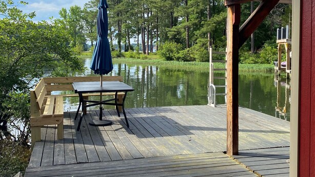 A wooden deck with a table and bench, overlooking a calm lake and dense trees. - Waterfront…Location is everything! (Littleton)