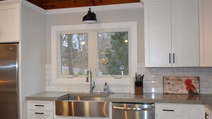 A modern kitchen with white cabinets, stainless steel appliances, and a window with a view of trees. - Waterfront…Location is everything! (Littleton)