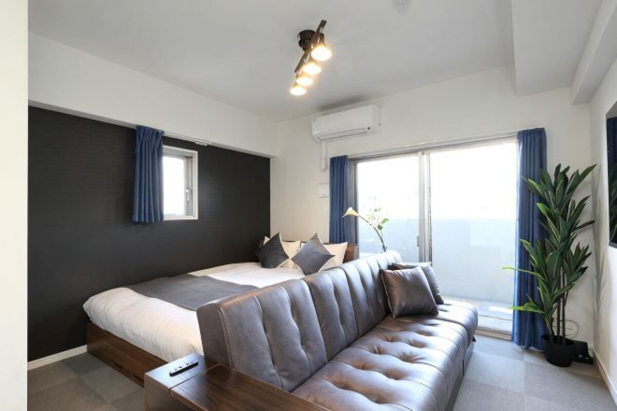 A modern hotel room with a bed, a sofa, a potted plant, and a large window.