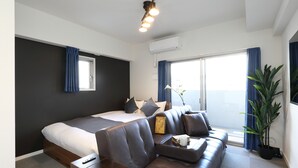 A modern hotel room with a large bed, a sofa, a small table, and a potted plant.