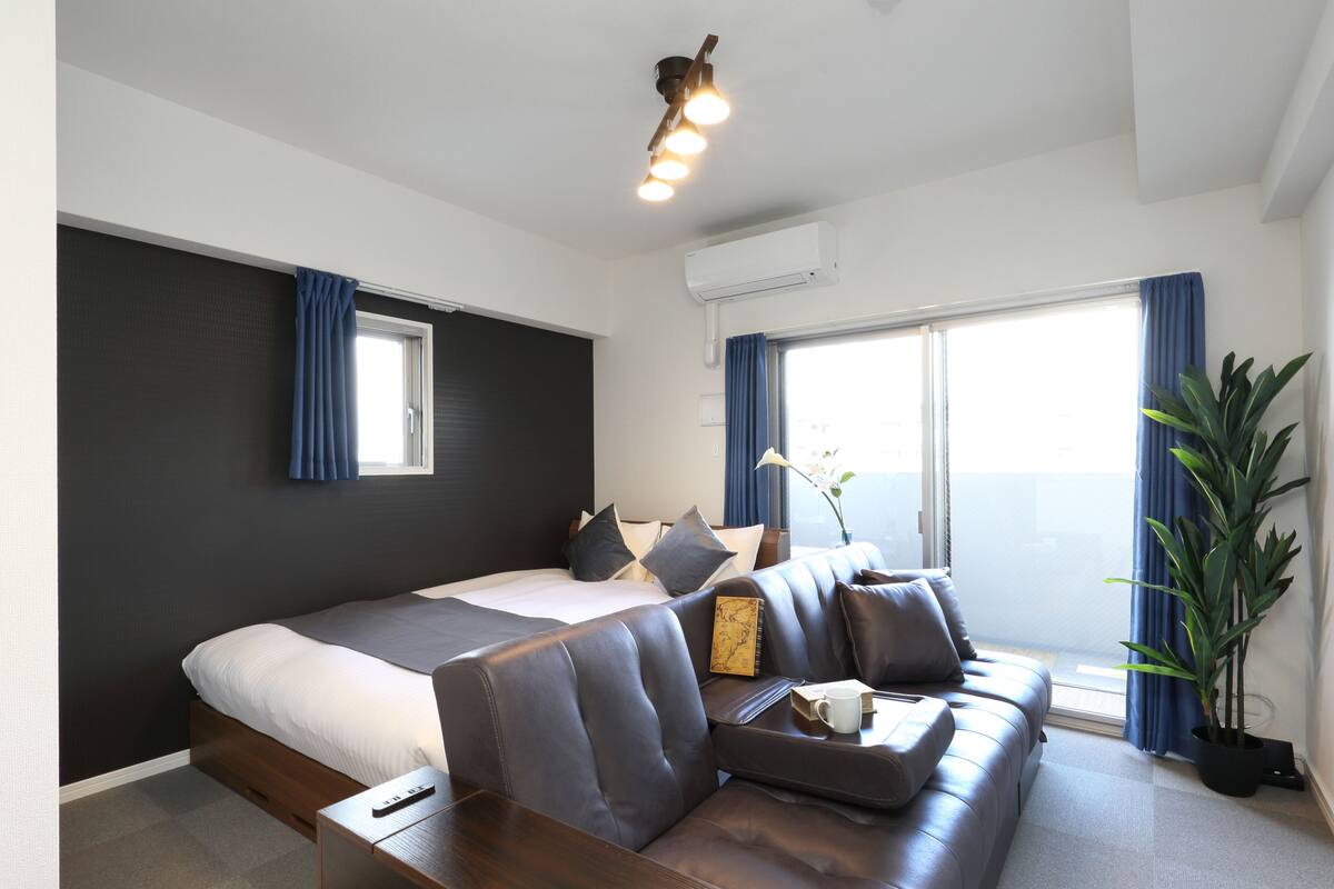 A modern hotel room with a large bed, a sofa, a small table, and a potted plant.