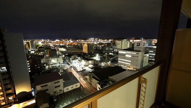 A nighttime cityscape viewed from a balcony with buildings, streets, and distant mountains.