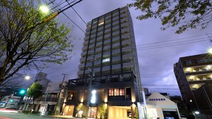 A multi-story building with a modern design, featuring a ground-level entrance with a sign, and a parking area visible in the foreground.