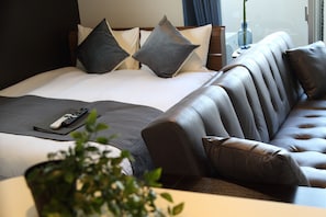 A modern hotel room with a large bed, a leather sofa, and a remote control on the bed.