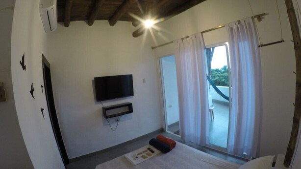 A bedroom with a bed, a flat-screen TV mounted on the wall, and a sliding glass door leading to an outdoor area.