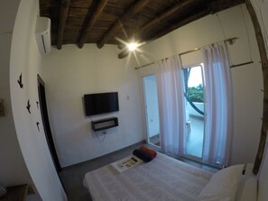A bedroom with a bed, a flat-screen TV mounted on the wall, and a sliding glass door leading to an outdoor area.