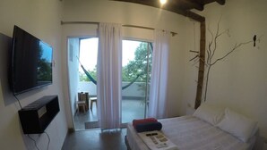 A bedroom with a bed, a TV, and a view of the outdoors through a glass door.