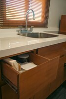 Una cocina con un lavamanos de acero inoxidable, armarios de madera y una ventana con persianas.