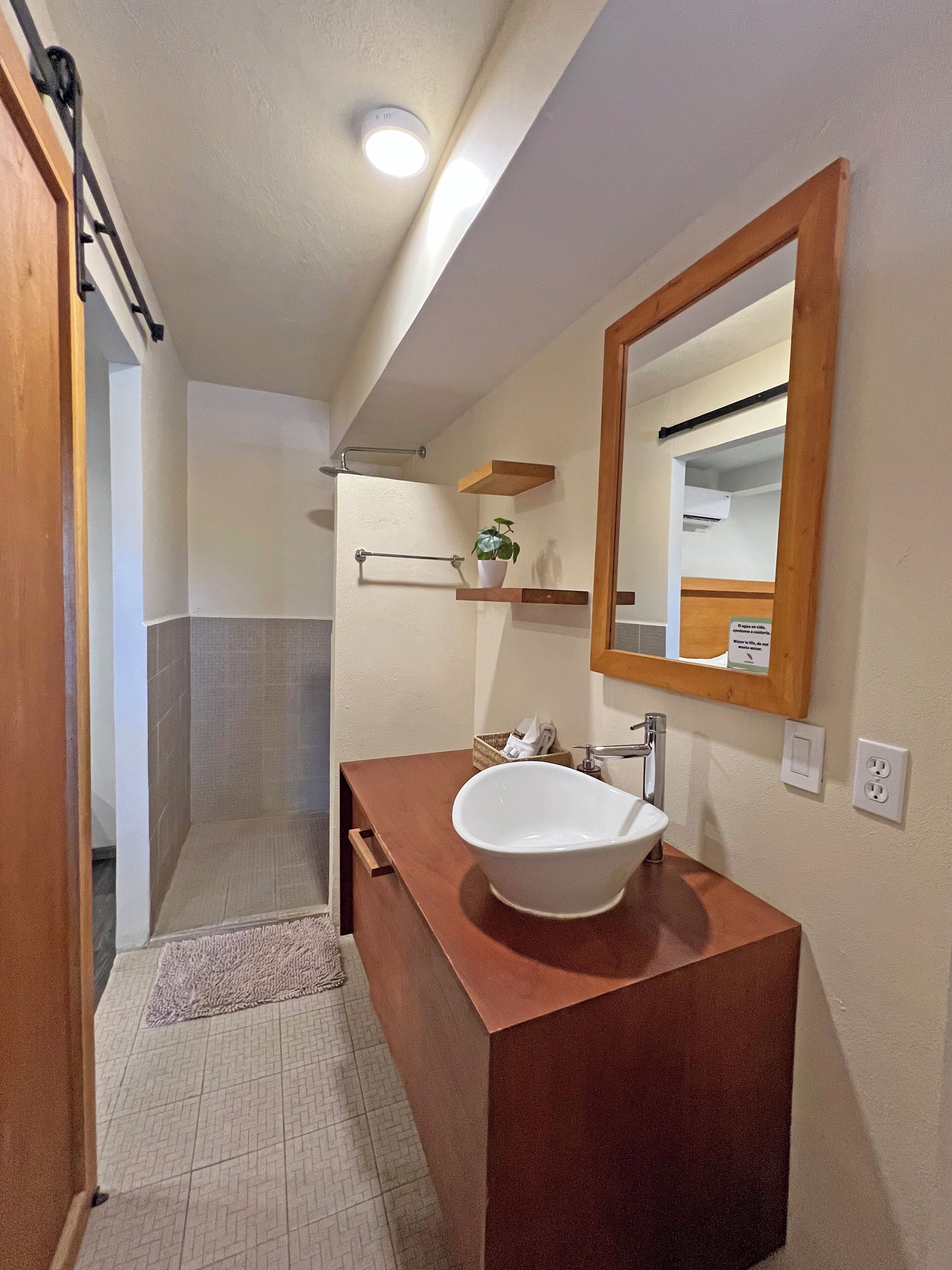 A bathroom with a wooden vanity, a white sink, a mirror, and a shower area.