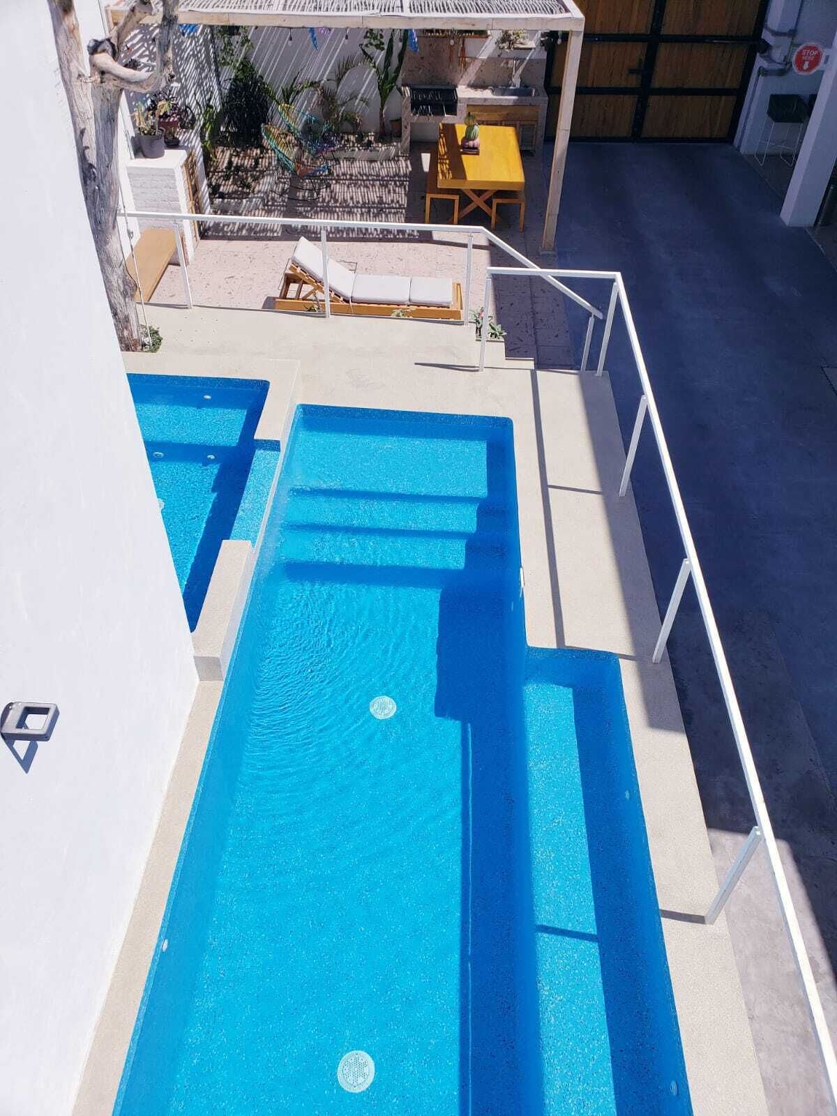 Una piscina en la azotea con agua azul cristalina, rodeada por una barandilla blanca y una terraza de madera.