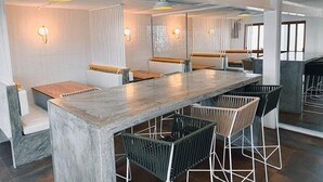 A modern dining area with a long table, multiple chairs, and wall-mounted lights. - Casa Palo Verde  (Cabo San Lucas)