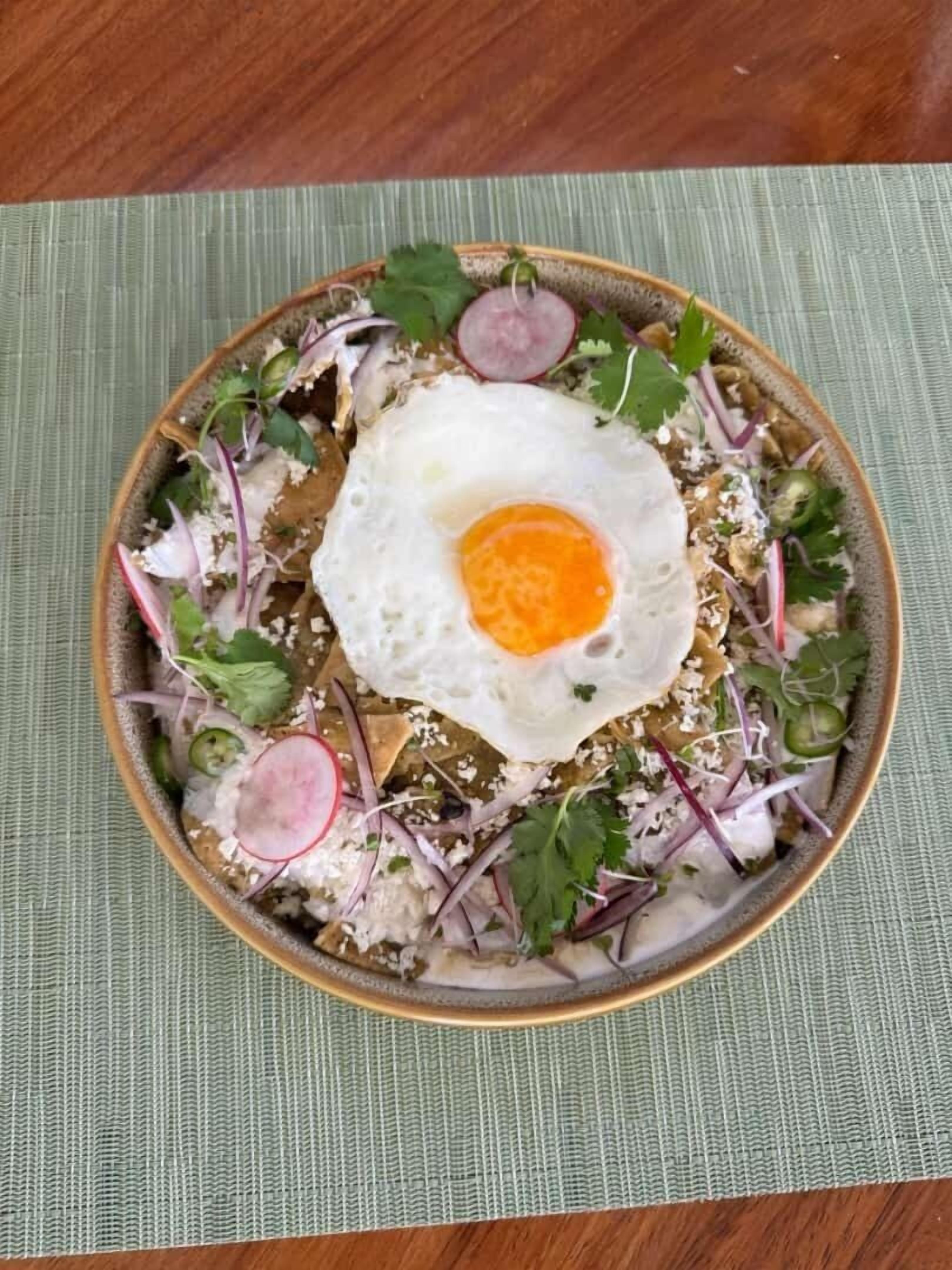 A bowl of food with a fried egg on top, surrounded by various vegetables and garnishes.