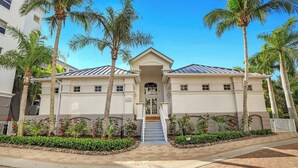 A two-story building with a central entrance, palm trees, and a paved walkway. - Regatta - Enjoy Gulf Views, Walk to the Beach! (Naples)