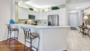 A modern kitchen with white cabinets, stainless steel appliances, and a central island with bar stools. - Regatta - Enjoy Gulf Views, Walk to the Beach! (Naples)