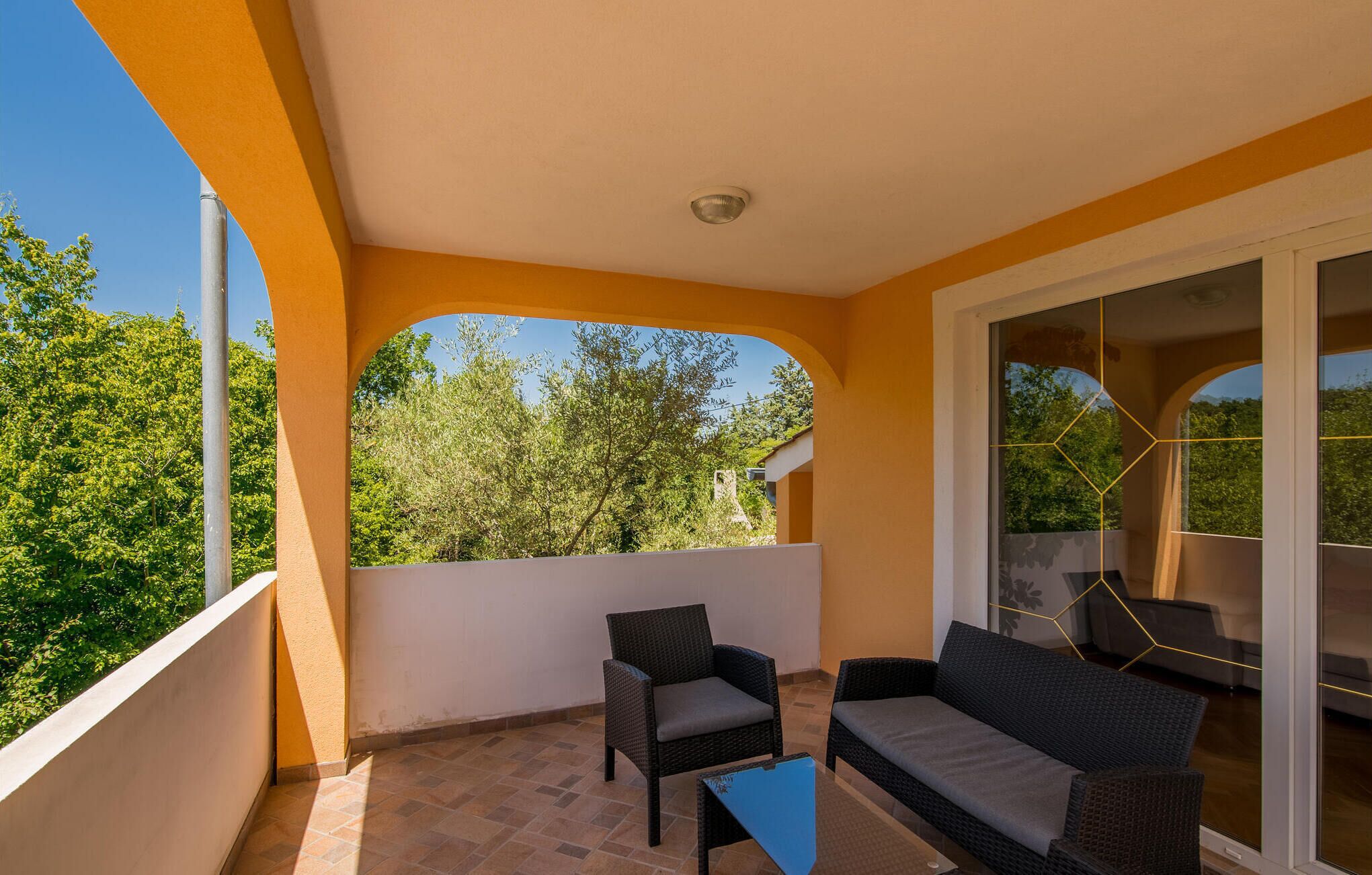 A balcony with a view of trees, a sofa, a chair, and a small table.