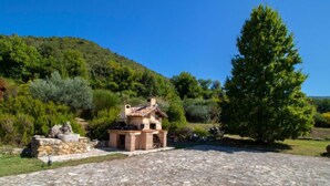A stone patio leading to a small stone building with a tiled roof, surrounded by lush greenery and a large tree. - La Danza by Interhome (Todi)