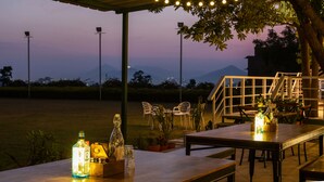 An outdoor seating area with tables and chairs, a bottle of liquor, and a staircase leading to an upper level. - The G Snoozebox (Udaipur)