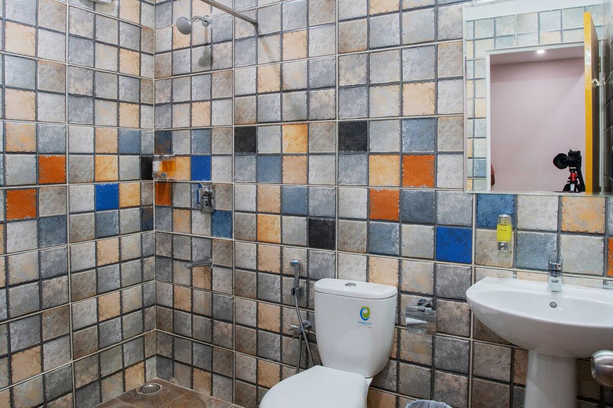 Un bagno con doccia, toilette e lavandino, rivestito di piastrelle multicolore.