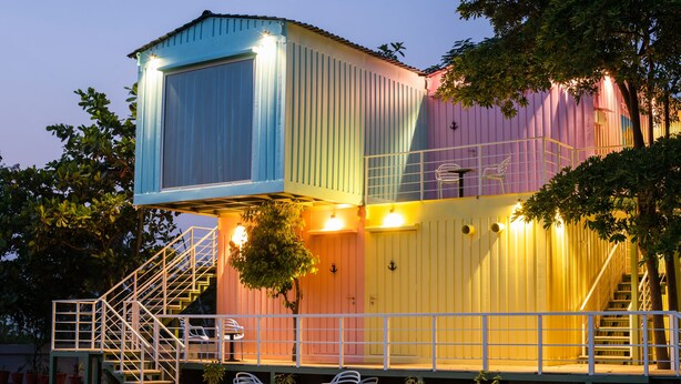 A colorful, multi-level outdoor structure with a staircase, seating area, and potted plants. - The G Snoozebox (Udaipur)
