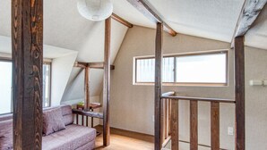A loft-style room with exposed wooden beams, a cushioned bench, and large windows.