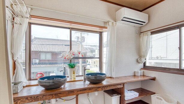 A compact kitchen with a wooden countertop, two bowls, a potted plant, and a view of traditional buildings through a large window.