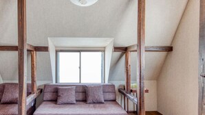 A bedroom with a loft bed, a window, and wooden beams.