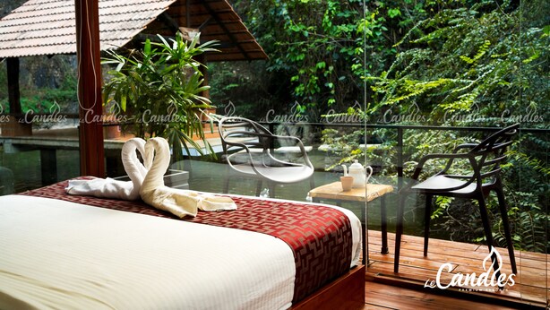 A bedroom with a bed, a glass table, two chairs, and a view of a lush garden. - Le Candles Resort (Kozhikode)