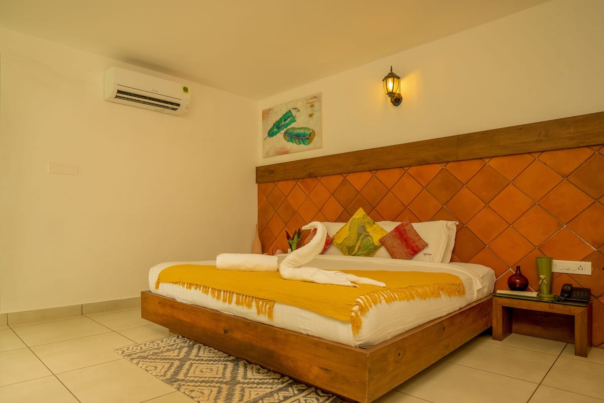 A bedroom with a wooden headboard, a bed with a yellow blanket, a bedside table with a vase, and a wall-mounted air conditioner.