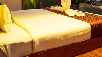 Een netjes opgemaakt bed met witte lakens, een geborduurde deken, een houten hoofdbord en een glazen scheidingswand.