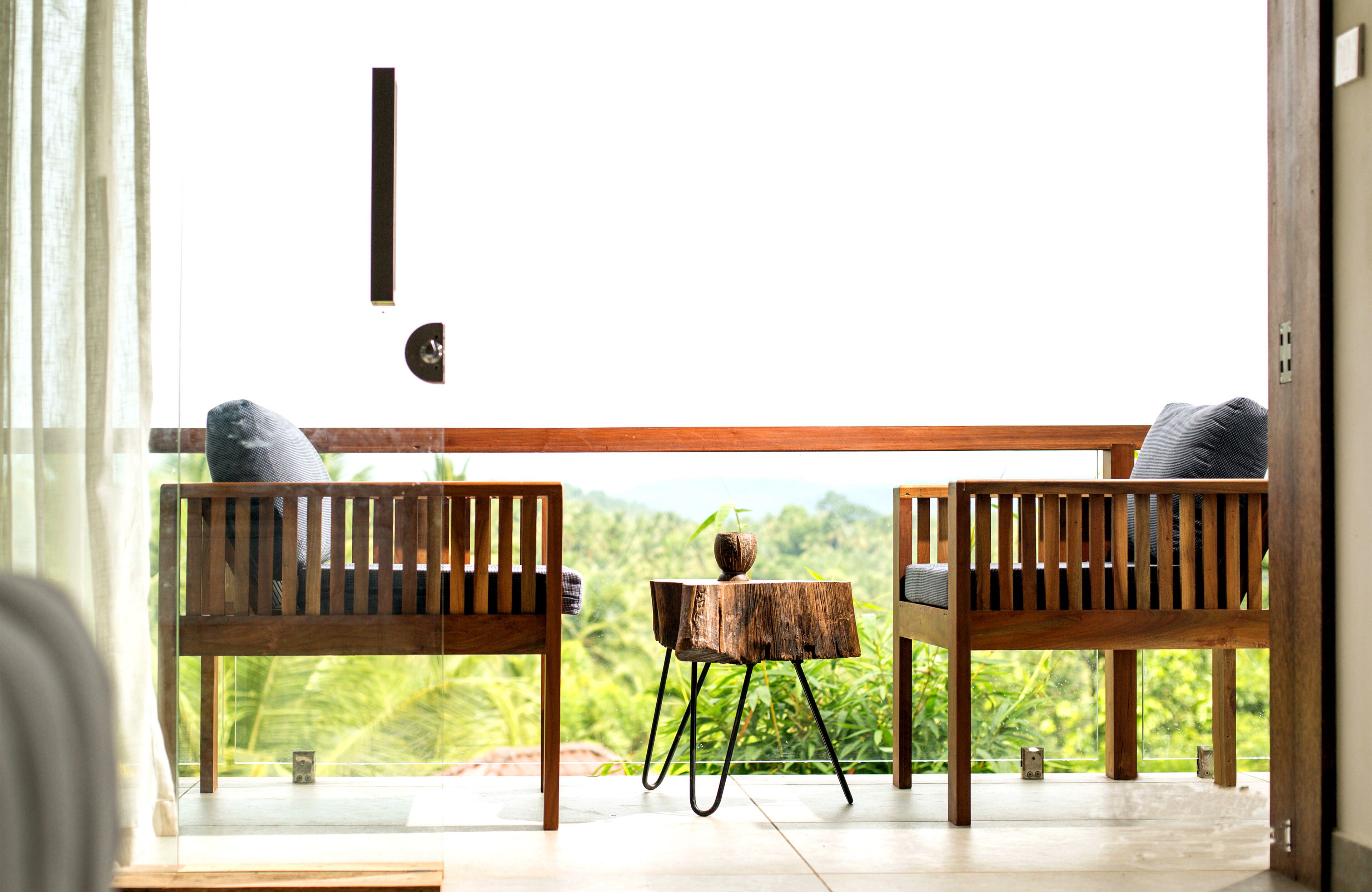 Una habitación con dos bancos de madera y una pequeña mesa de madera, vista a exuberante follaje en el exterior, y un ventanal grande.