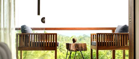 Una habitación con dos bancos de madera y una pequeña mesa de madera, vista a exuberante follaje en el exterior, y un ventanal grande.