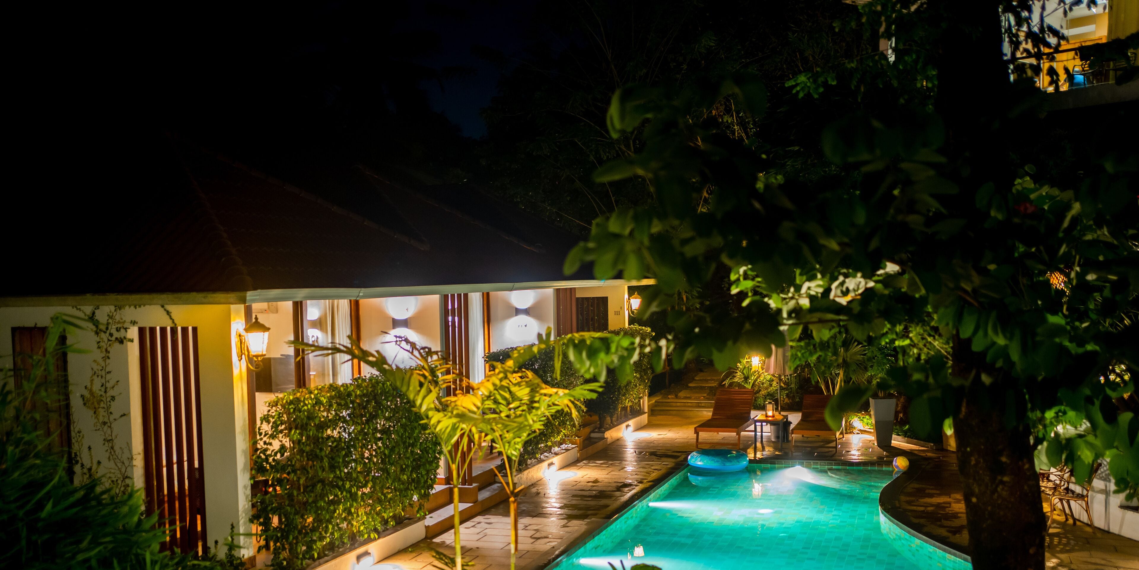 A nighttime view of a pool area with a lounge chair, a small table, and a potted plant.