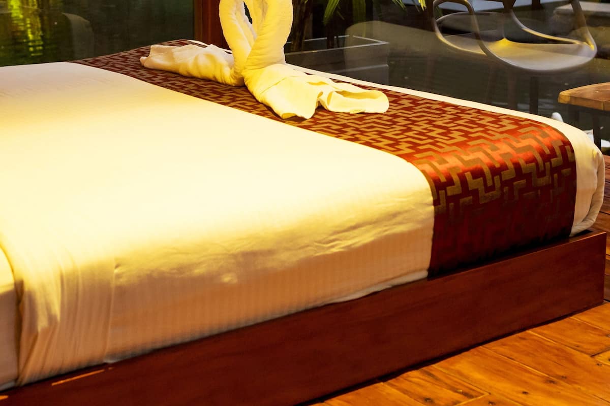 A neatly made bed with a patterned bedspread and pillows, a wooden headboard, and a glass table beside the bed.