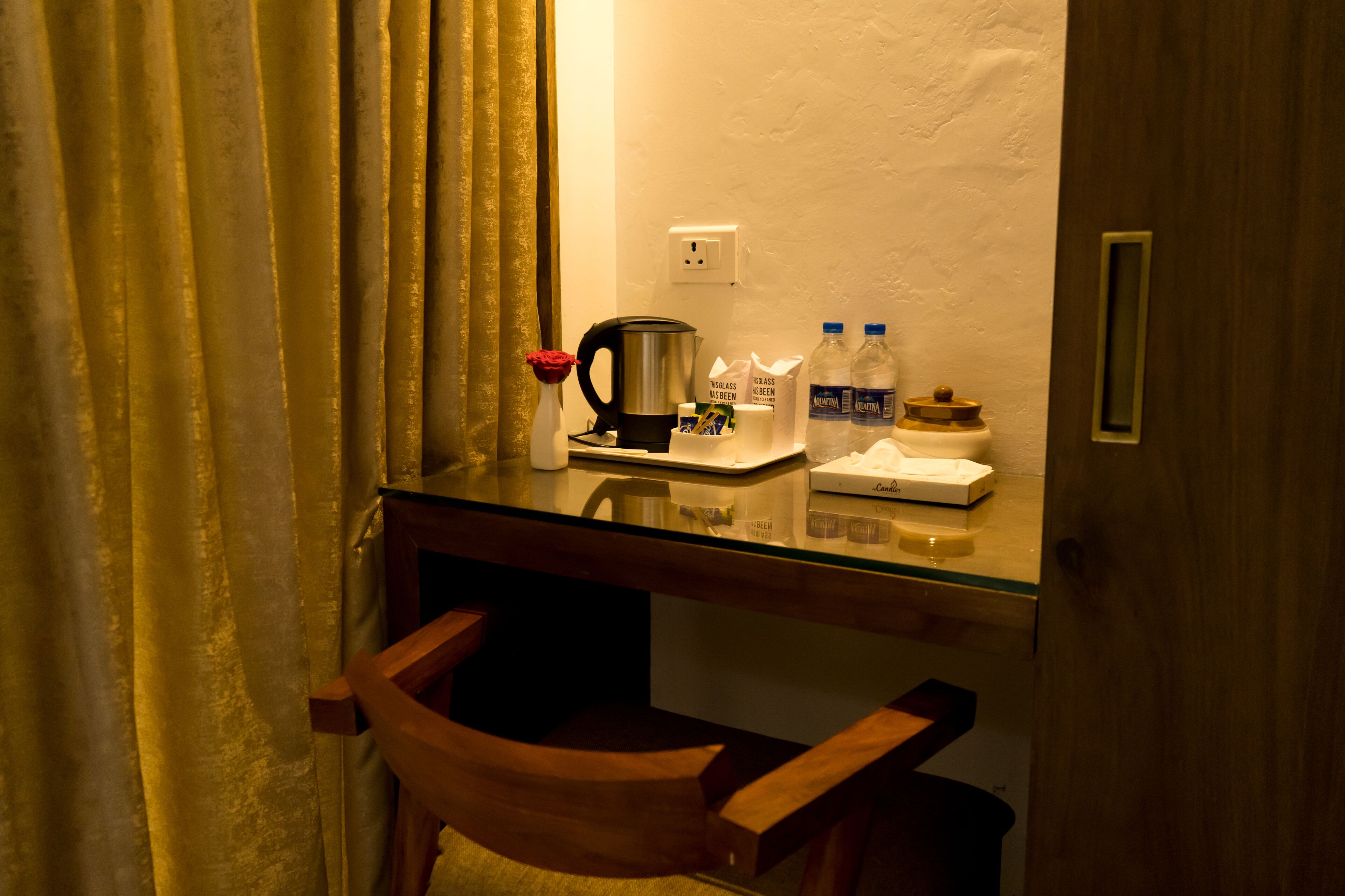A hotel room with a glass desk, a coffee maker, a bottle of water, and a tissue box.