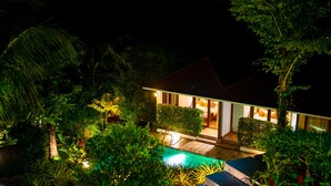 A modern house with a pool, surrounded by lush greenery at night. - Le Candles Resort (Kozhikode)