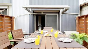 An outdoor dining area with wooden tables and chairs, set against a building with a grey facade. - Dekijima Sakura House (Osaka)