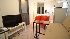 A modern living room with a flat-screen TV, a glass-top coffee table, a sofa, and a refrigerator. - Dekijima Sakura House (Osaka)